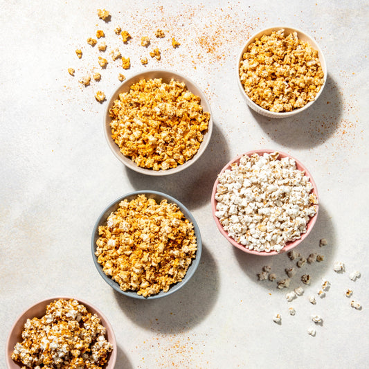 Five colorful bowls filled with different popcorn flavors—caramel, cheese, and plain—are artfully arranged on a light surface.