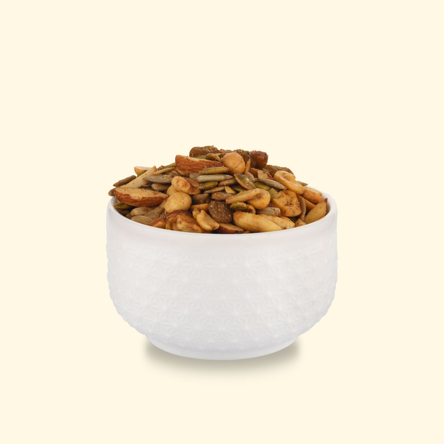 A textured white bowl overflows with a colorful mix of nuts and seeds, set against a soft yellow background for a healthy snack.